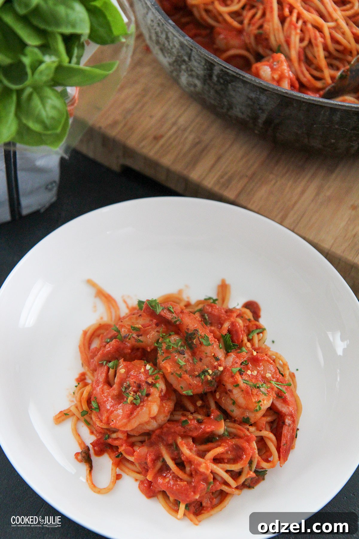 a white bowl with spaghetti and shrimp and basil on the side 