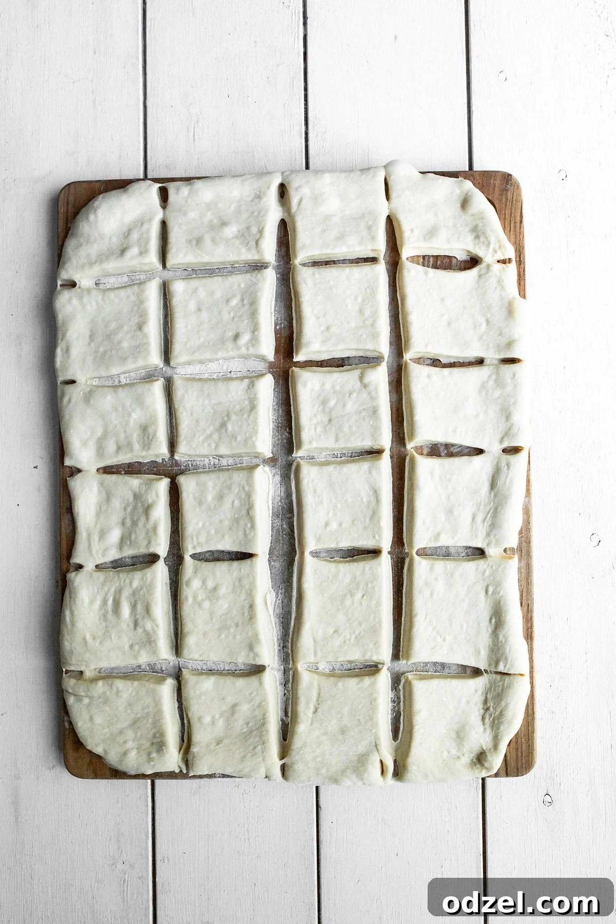 Pillowy Soft Beignet Delights 3 Twenty-four perfectly cut squares of raw beignet dough arranged neatly on a wooden cutting board, ready for frying.