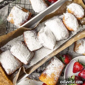 Pillowy Soft Beignet Delights 6 A long brown paper bag filled with hot, freshly fried beignets. More beignets are scattered around the bag, alongside vibrant fresh strawberries and blueberries, creating an inviting display.
