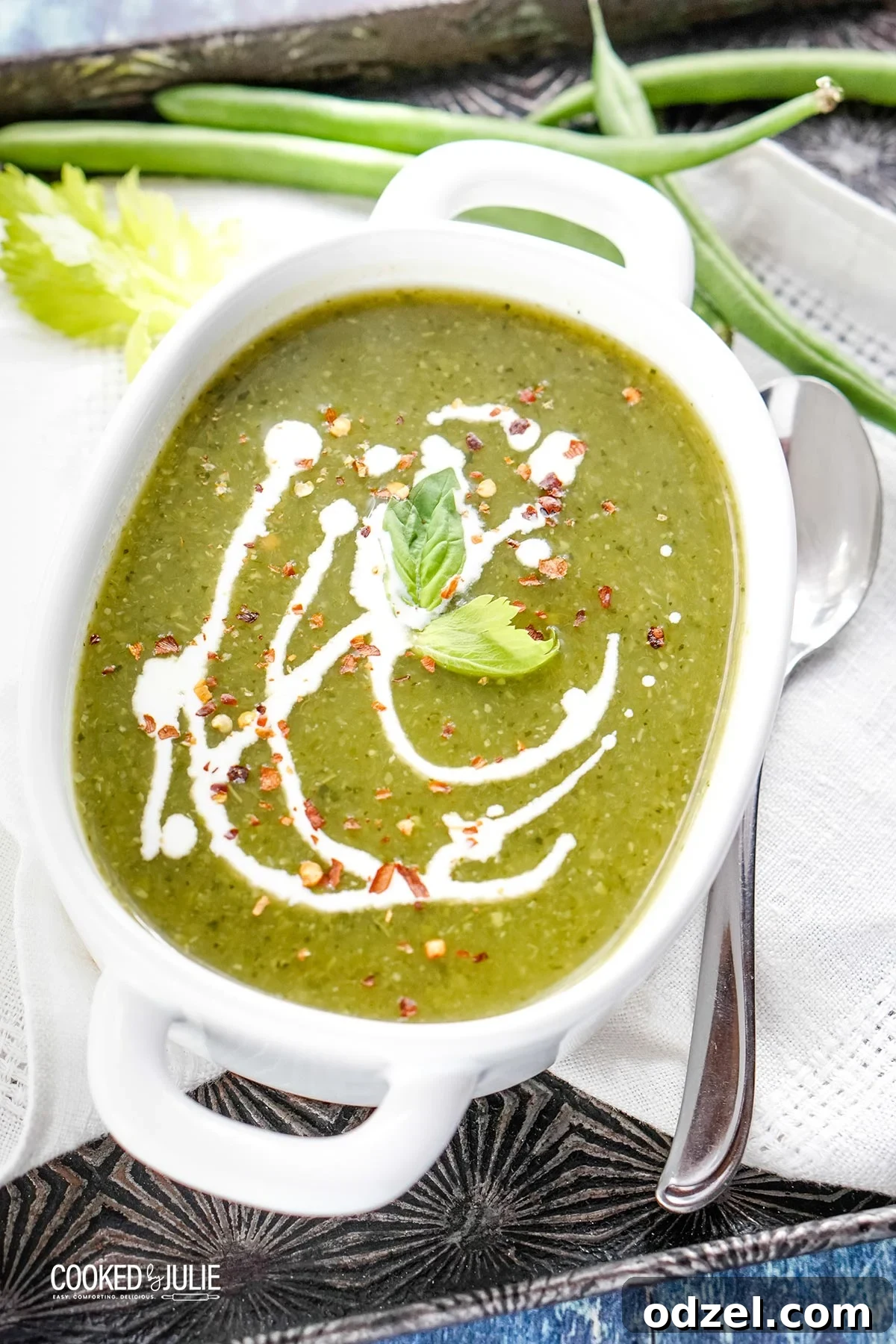 Creamy vegan green detox soup in a white bowl, garnished with a swirl of coconut milk and fresh basil