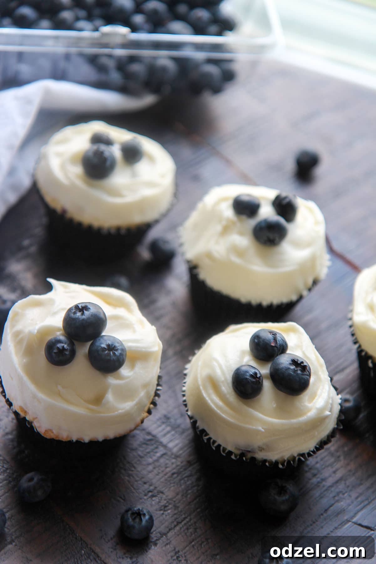 Blueberry Cloud Cupcakes 5 Four beautifully frosted blueberry cupcakes garnished with fresh blueberries, on a white plate