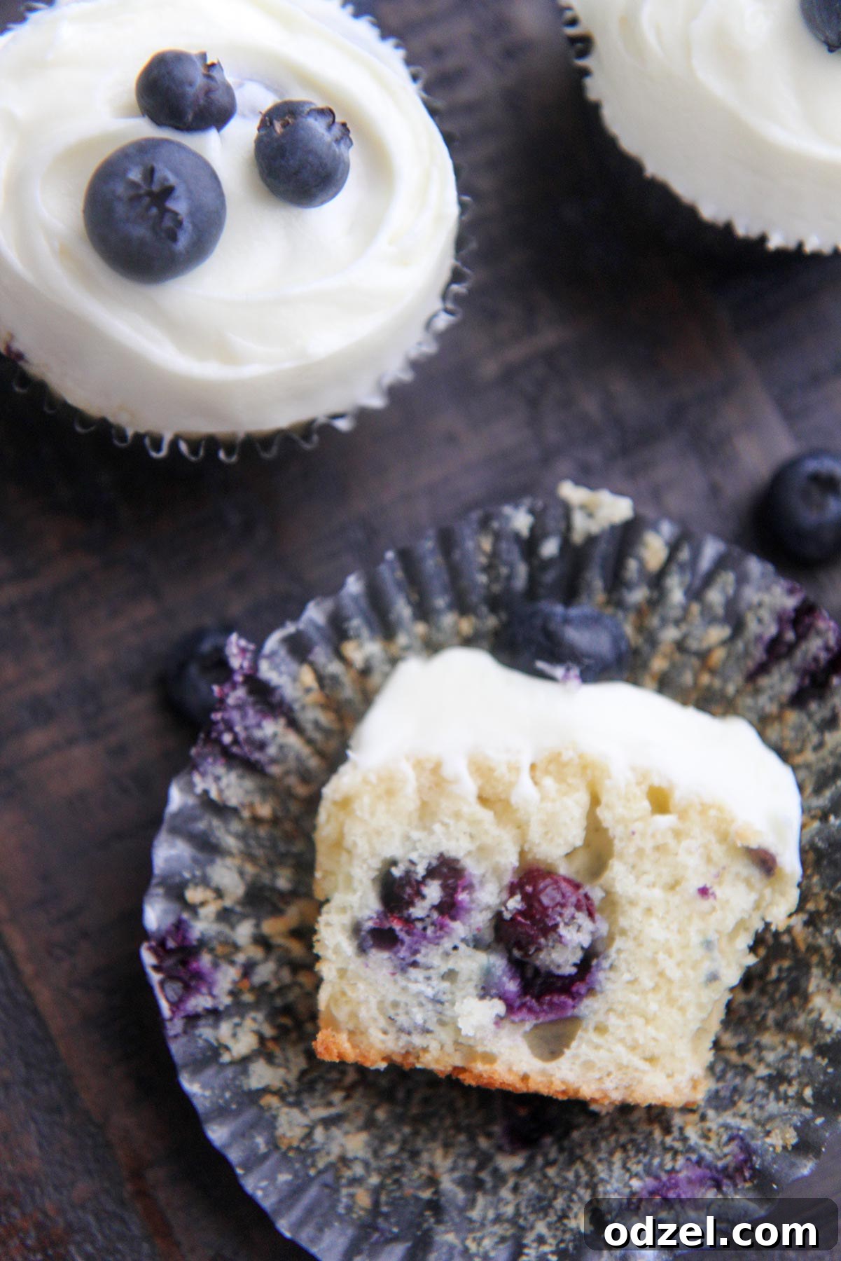 Blueberry Cloud Cupcakes 6 Close-up of a half-eaten blueberry cupcake, revealing its moist interior and juicy blueberry pieces