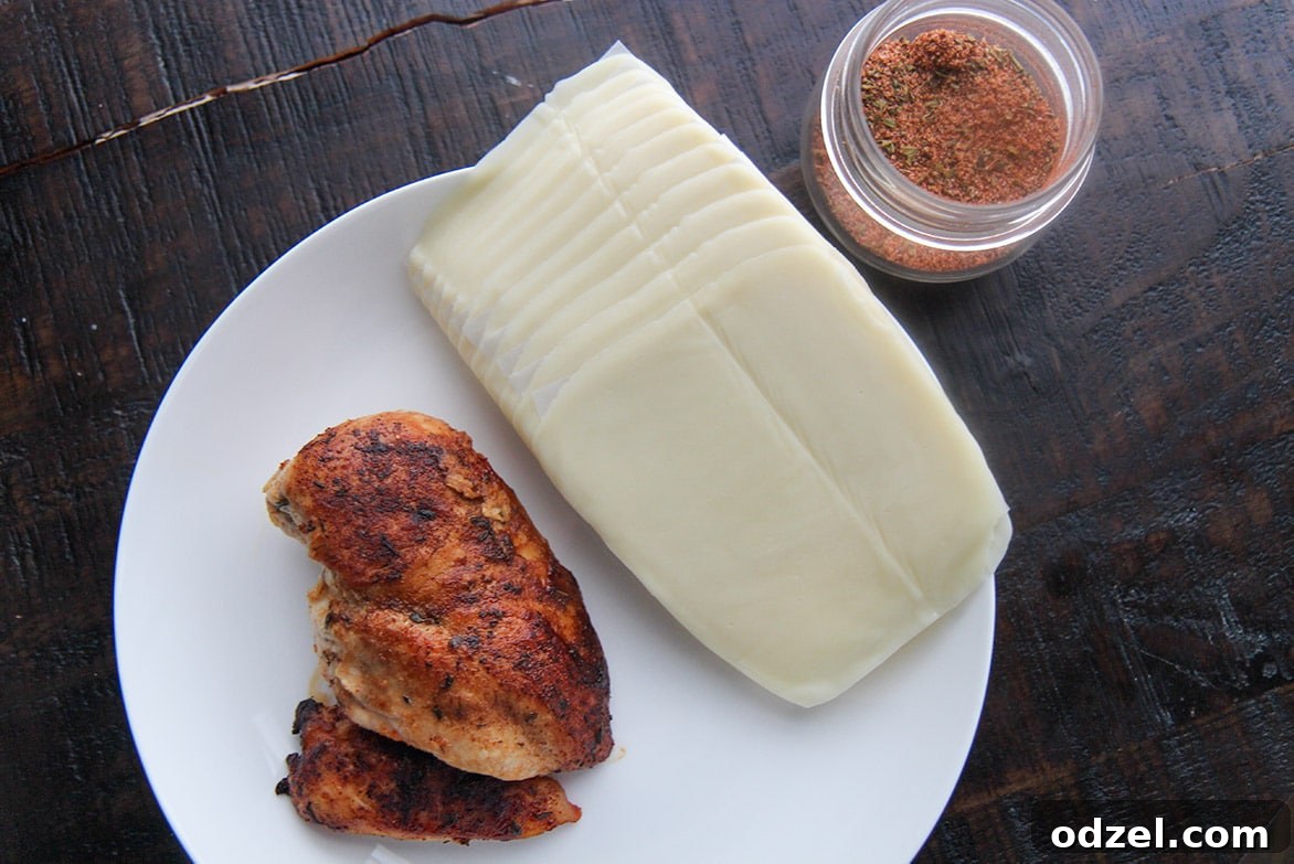 Three core ingredients: cooked chicken breast, a jar of flavorful Cajun seasoning, and a stack of mozzarella cheese slices, laid out on a clean surface.