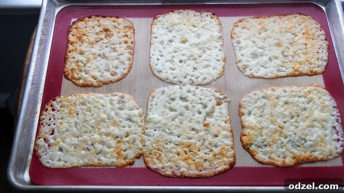 Six perfectly melted mozzarella cheese slices, golden and pliable, arranged on a silicone mat on a baking sheet, forming the base for the taquitos.
