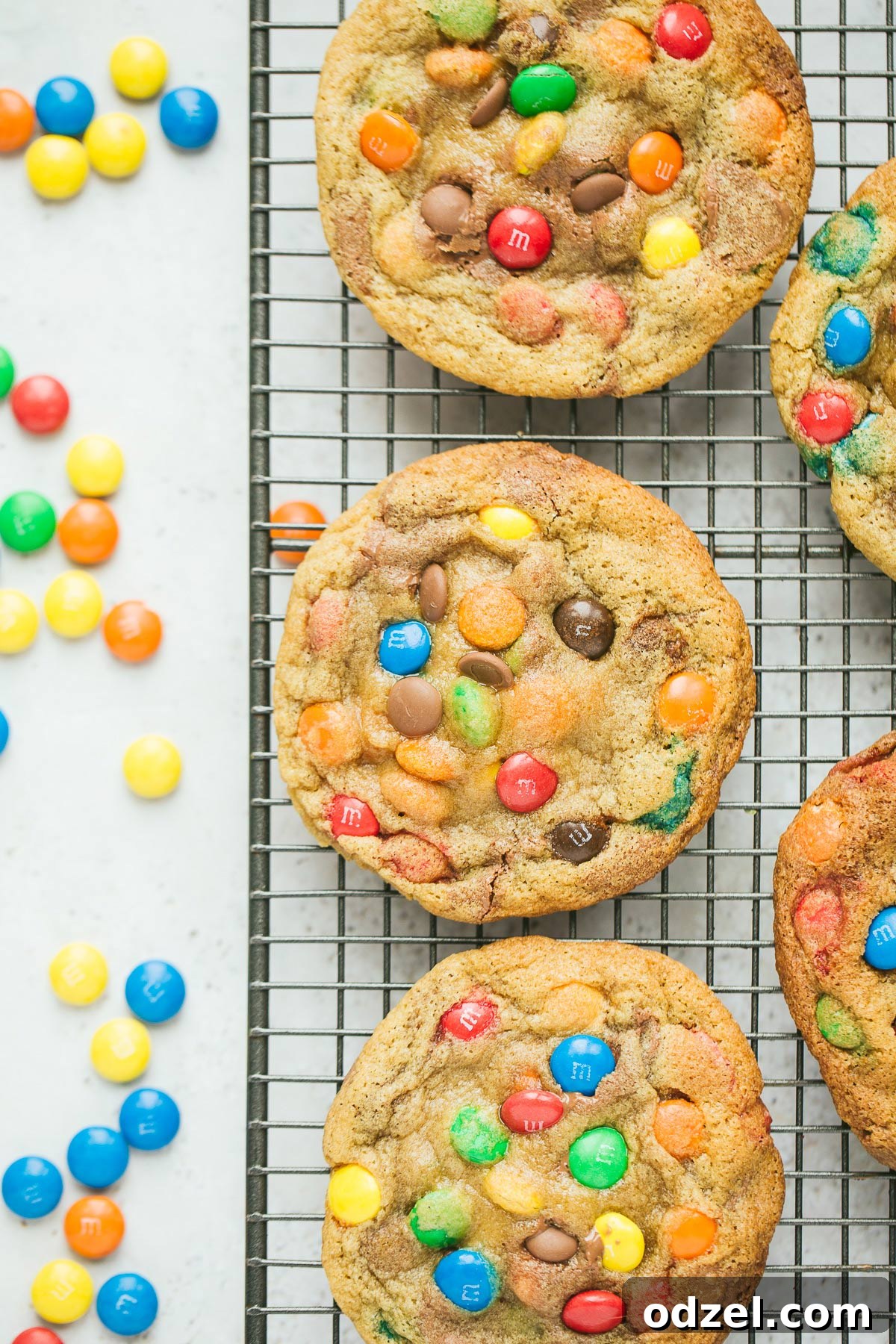 Irresistible M&M Cookies 2 Five vibrant M&M cookies cooling on a wire rack, with a scattering of colorful M&M candies beside them, inviting you to indulge in this classic treat.