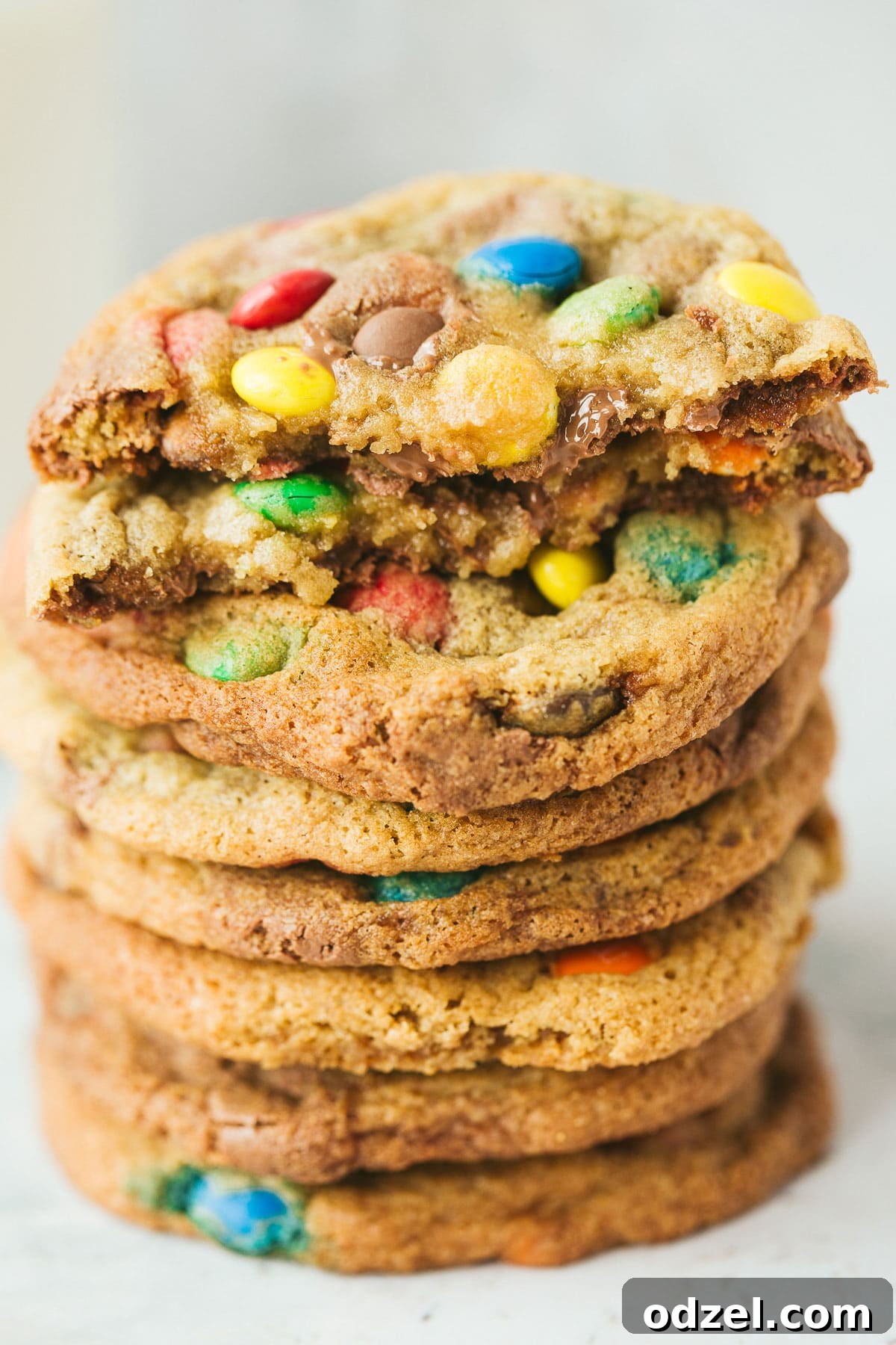 Irresistible M&M Cookies 4 Eight vibrant M&M cookies stacked in a delicious tower, with one cookie cut in half to reveal its soft, chewy interior filled with melted chocolate and M&M's.