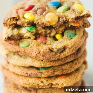 Eight M&M cookies stacked, with one cut in half, showcasing their delicious interior.