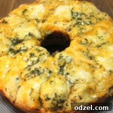 A warm Cheesy Garlic Monkey Bread, freshly baked, with a rustic golden-brown exterior and bubbling melted cheese peeking through, presented in a round form.