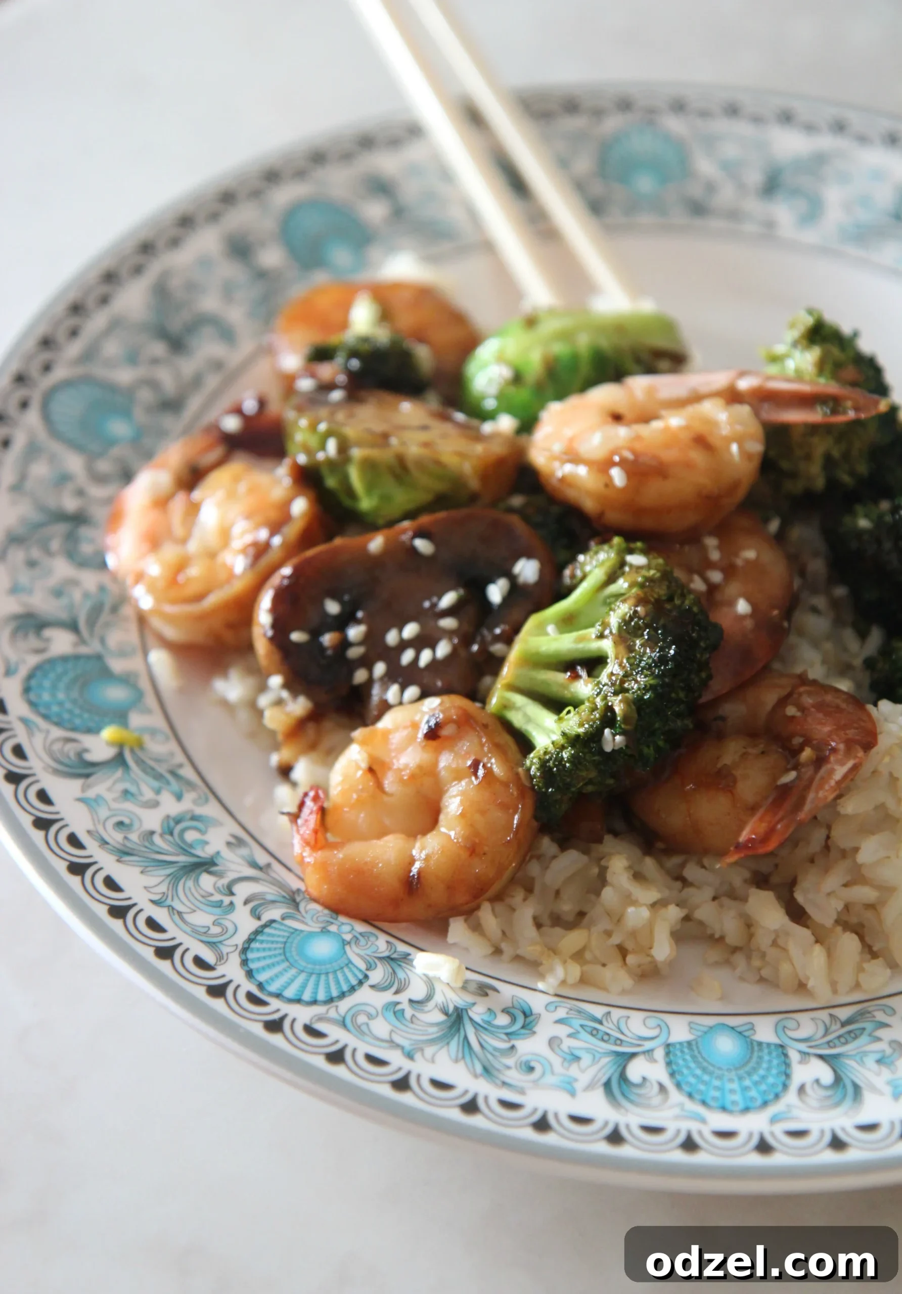 A beautifully plated shrimp, mushroom, and broccoli stir-fry served with rice, accompanied by chopsticks.