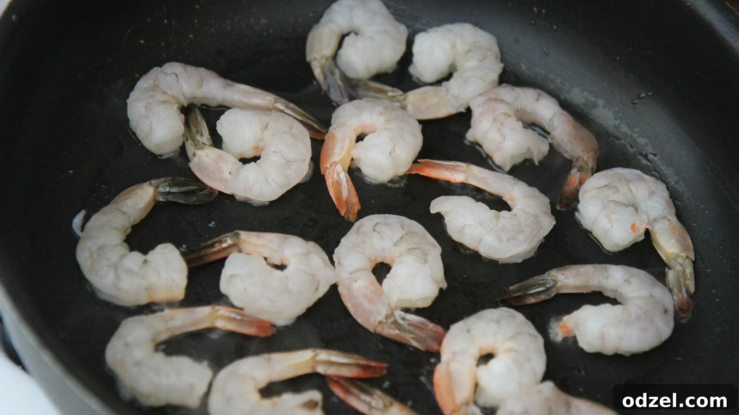 Raw, peeled, and deveined shrimp sizzling and turning pink in a hot black skillet, indicating readiness for the next step.
