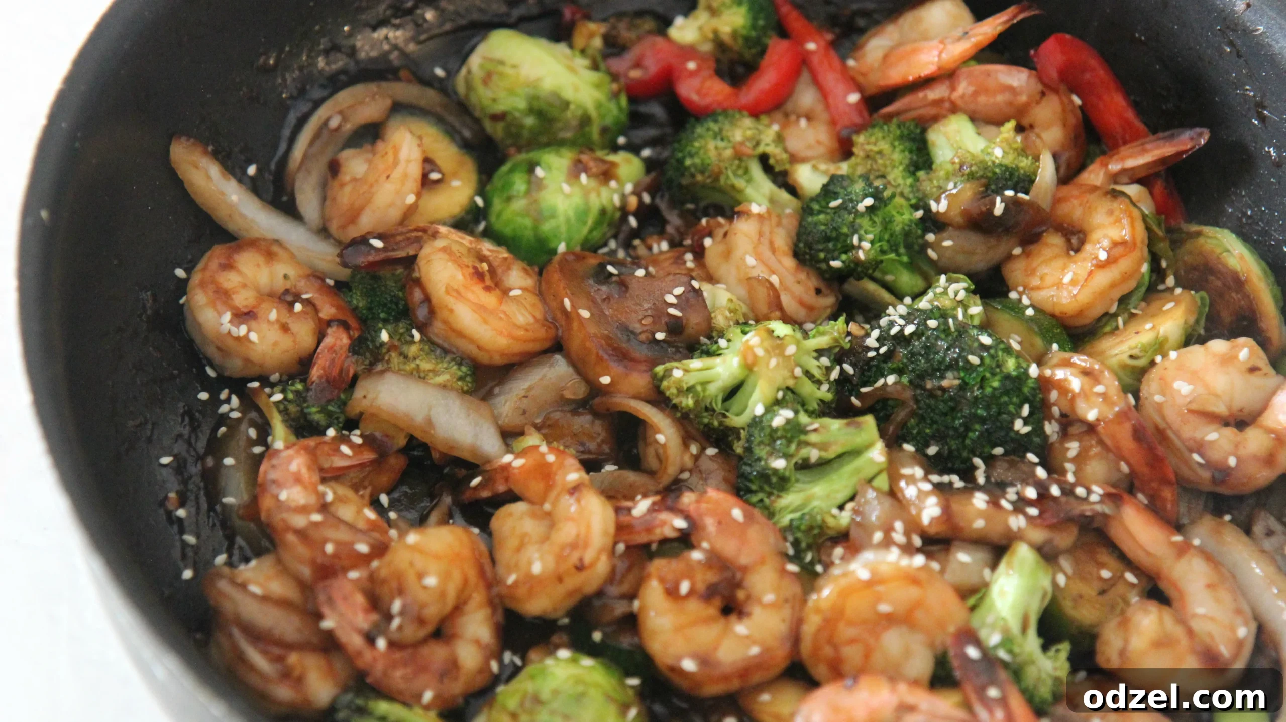A vibrant and perfectly cooked shrimp and vegetable stir-fry, glistening with a glossy, flavorful sauce, showcased within a black skillet, ready to be served.