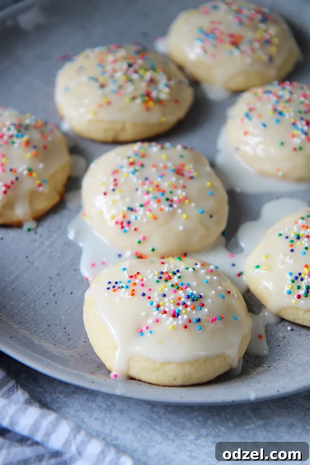 Sunshine-Kissed Lemon Ricotta Bites 2 Seven Italian lemon ricotta cookies with a glaze and sprinkles on a gray plate, showcasing their soft, round shape and vibrant topping.