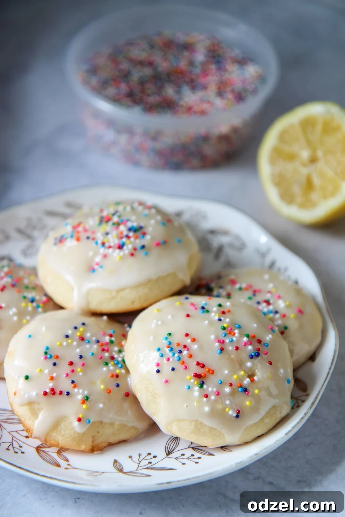 Sunshine-Kissed Lemon Ricotta Bites 6 Soft baked Italian lemon ricotta cookies on a small plate with colorful sprinkles, a fresh lemon, and a sprig of mint in the background.