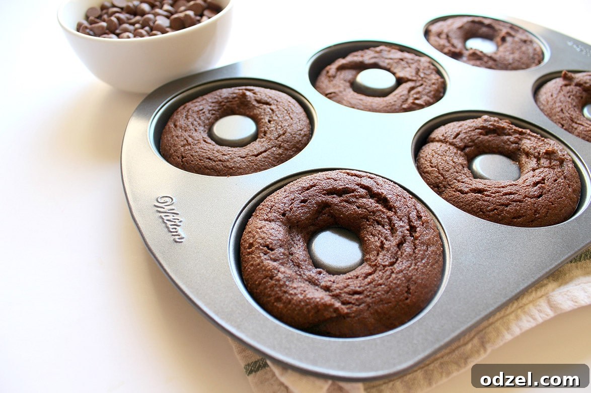 A six-cavity donut pan filled with perfectly baked, golden-brown donuts, still in their molds, showcasing their uniform shape and inviting texture.