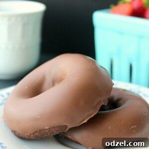 Two keto baked chocolate donuts on a white plate with a basket of strawberries in the background.
