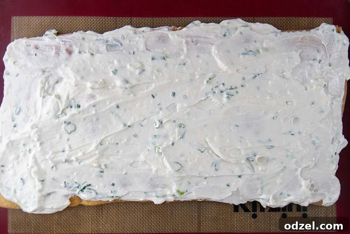 A freshly baked crescent roll crust completely covered with an even layer of seasoned cream cheese mixture, patiently waiting for the vibrant vegetable topping.