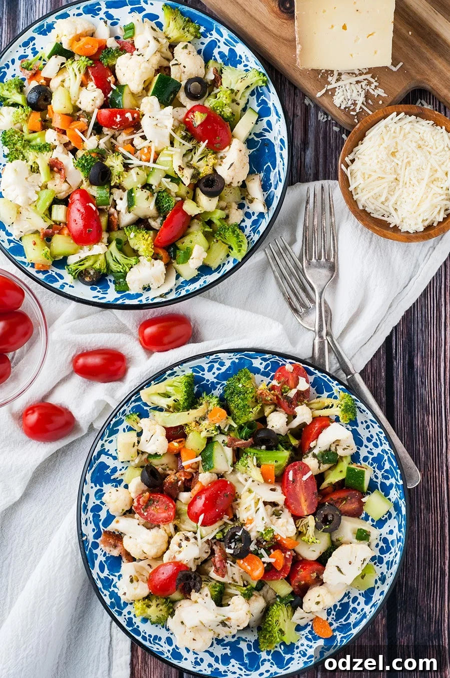 Two bowls brimming with colorful vegetable salad and homemade Italian dressing. Two forks are placed beside the bowls, with a sprinkle of Parmesan cheese.