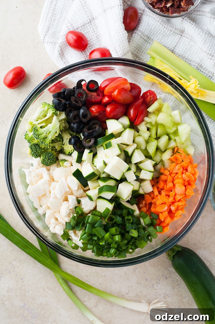 A large bowl showcasing a colorful array of raw vegetables including carrots, zucchini, broccoli, black olives, tomatoes, and cauliflower.
