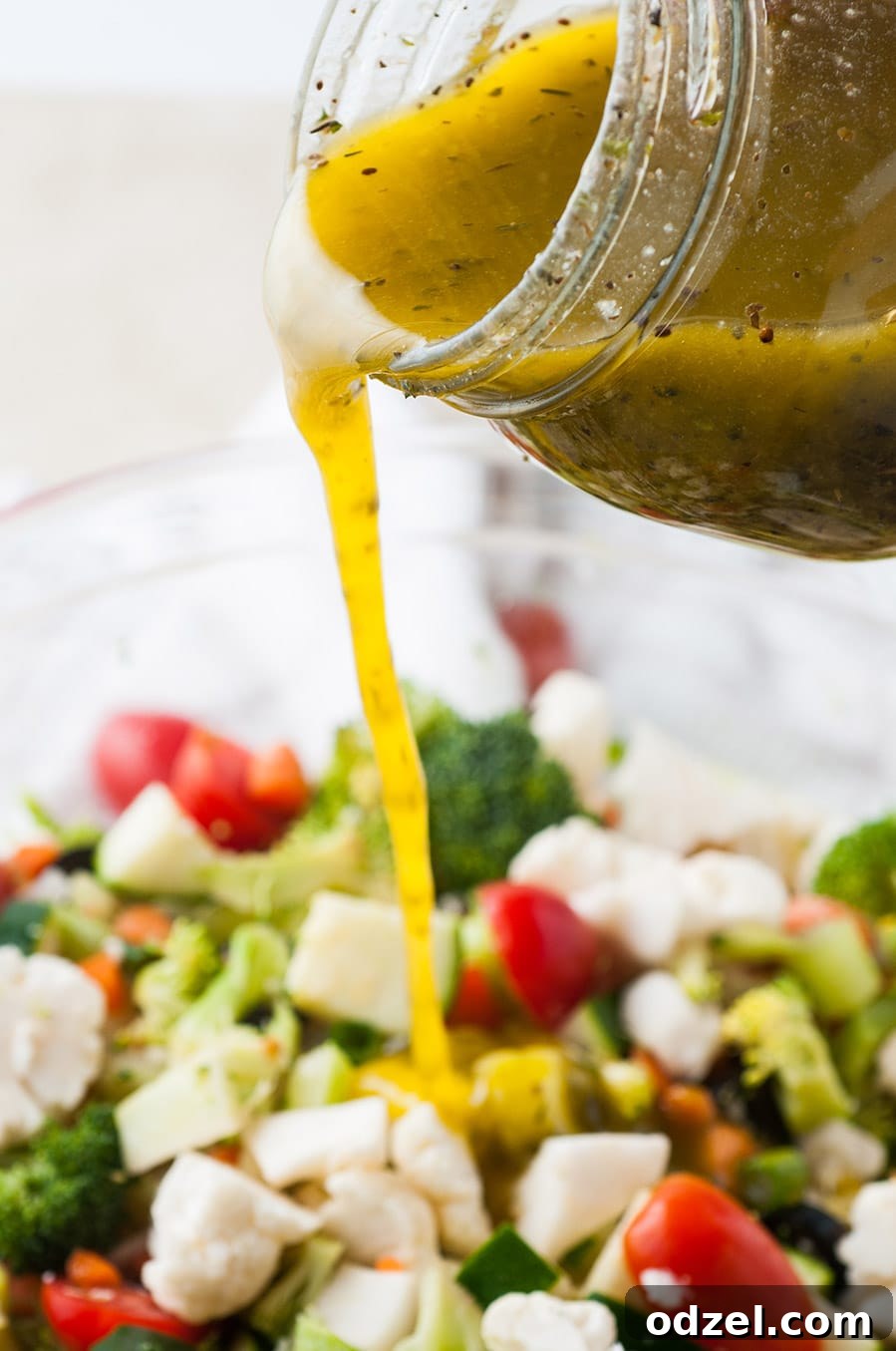 Homemade Italian dressing being poured over a large bowl of fresh vegetable salad.
