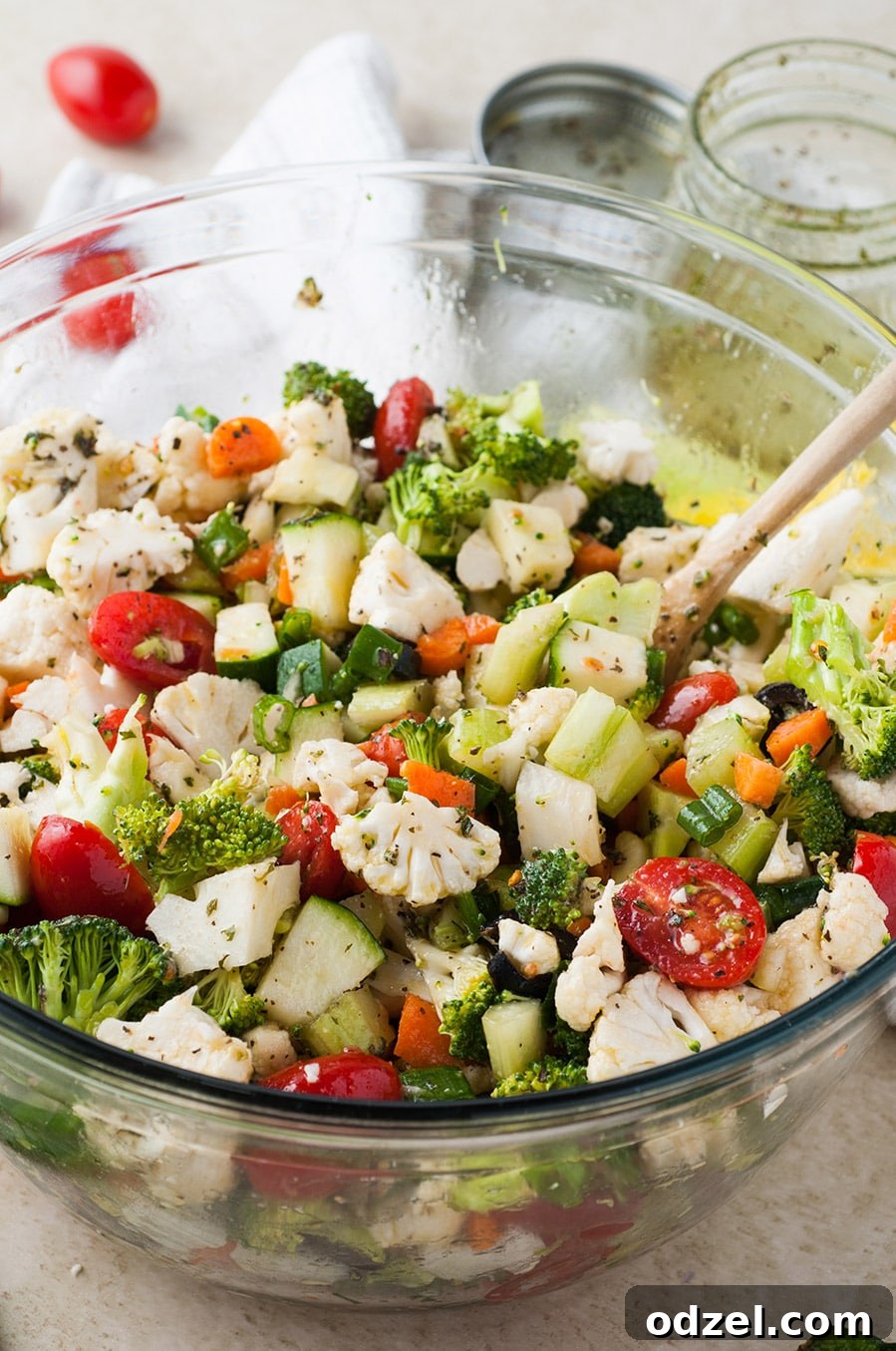 A bowl filled with a vibrant assortment of colorful raw vegetables, accompanied by a wooden spoon for serving.