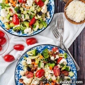 Two bowls filled with crunchy vegetable salad and homemade Italian dressing. Two forks on the side and parmesan cheese.