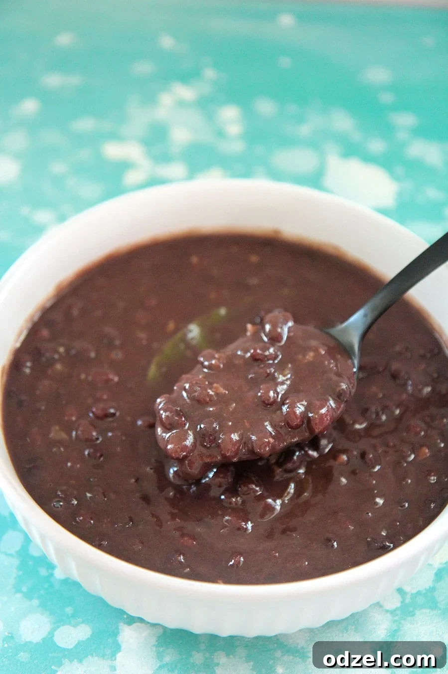 Flavorful Instant Pot Cuban Black Beans 2 Cuban black beans in a white bowl with a black spoon. On top of a blue and white surface.