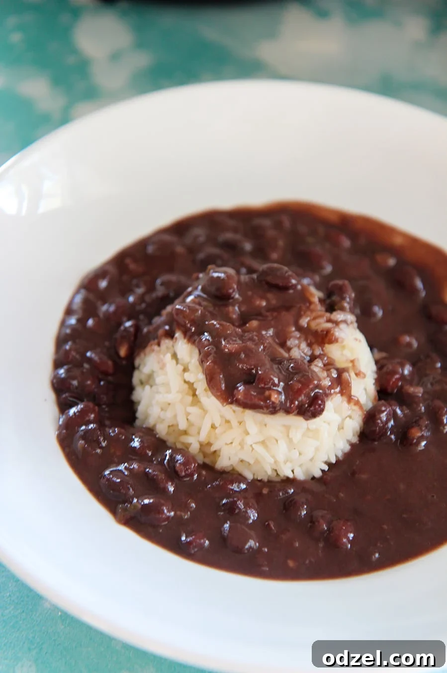 Flavorful Instant Pot Cuban Black Beans 4 black beans and white rice in a white bowl on top of a blue surface.