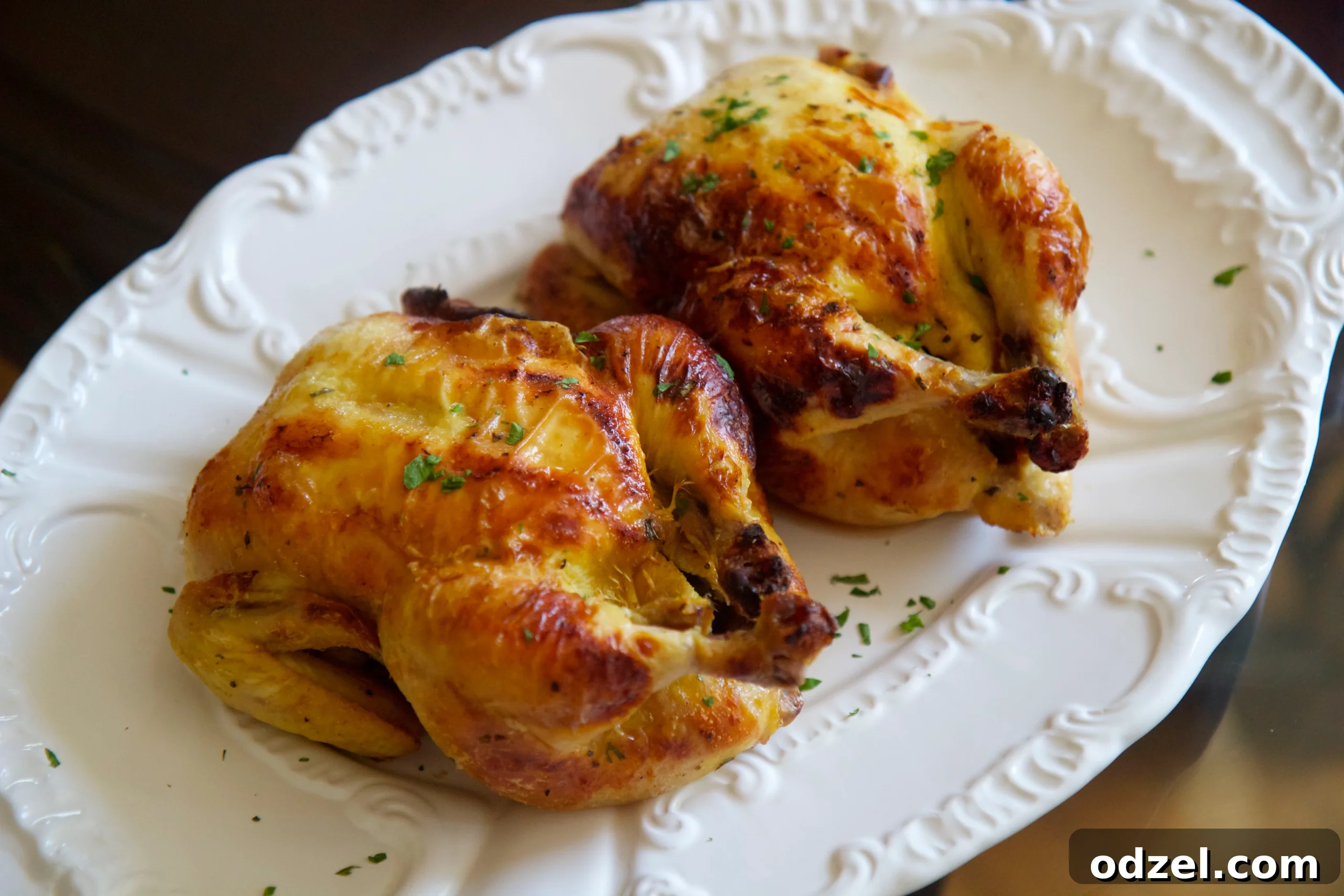Two golden-brown buttermilk brined Cornish Game Hens resting on a platter, garnished with fresh herbs, ready to be served. A perfect crowd-pleaser for any gathering.