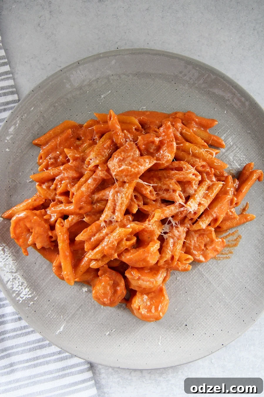 Penne alla vodka with shrimp on a gray plate with a gray and white towel on the side, showcasing its rich, creamy texture and succulent shrimp.
