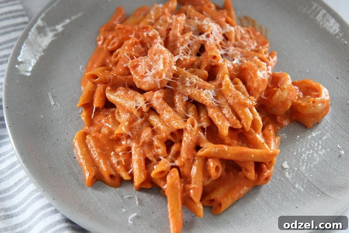 Close-up of creamy Penne alla Vodka with shrimp, sauce, and parmesan cheese on a gray plate, highlighting its appetizing details.