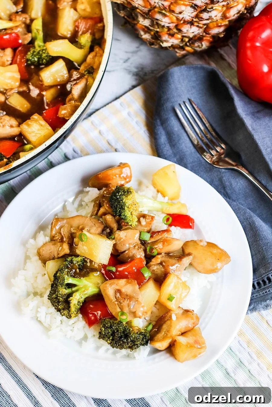 Sweet & Tangy Pineapple Chicken Stir-Fry 2 A beautifully plated pineapple chicken stir-fry served over fluffy white rice, with a fork ready on the side, and a blurred image of a skillet in the background, hinting at the culinary journey just completed.