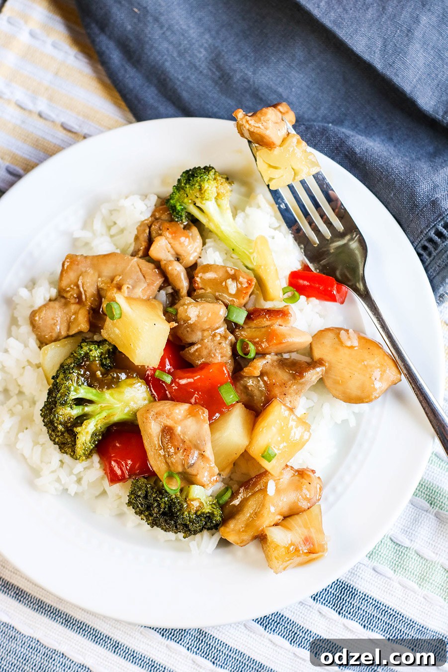 Sweet & Tangy Pineapple Chicken Stir-Fry 3 A close-up shot of a vibrant chicken and pineapple stir-fry served alongside fluffy white rice on a clean white plate, with a fork poised for a delicious bite. The ingredients, including chicken, colorful vegetables, and juicy pineapple, are clearly visible.