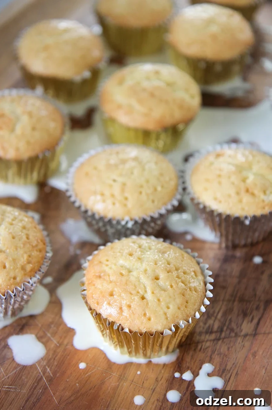 Nine perfectly soaked tres leches cupcakes, some with milk visibly absorbed into their bases, arranged on a textured wooden surface.