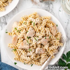Chicken and pasta in a white bowl with a fork and a blue towel on the side.