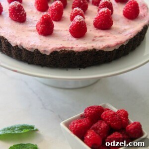 no-bake white chocolate raspberry tart on a white platter with a side of fresh raspberries and mint.
