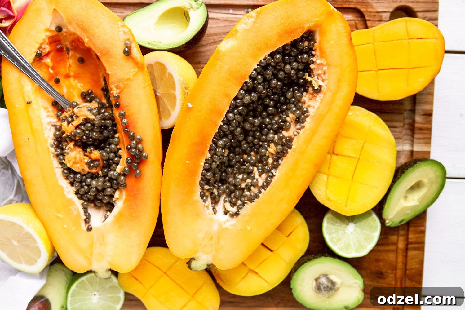 Layered Ethiopian Spris 4 A vibrant half-cut papaya, showcasing its juicy orange flesh and seeds, rests on a rustic wooden board, flanked by a ripe mango and a creamy avocado, hinting at the fresh ingredients for an Ethiopian Spris.