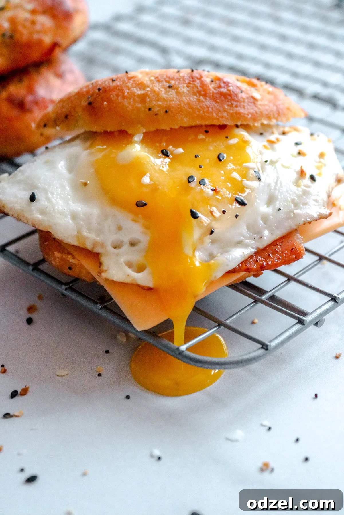 An intimate, close-up view of the keto breakfast sandwich, revealing a perfectly runny egg yolk cascading over the crispy bacon and melted cheese, all resting on a wire rack.