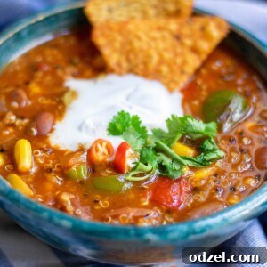 A bowl with quinoa chili, white cream on top, cilantro, and dorito chips on top of a blue towel.