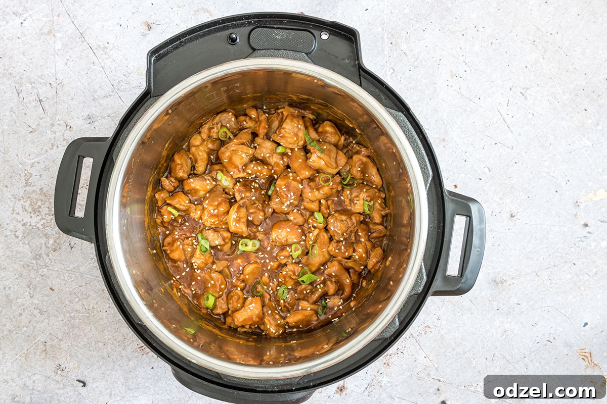 Close-up shot of sesame chicken with chopped scallions inside an Instant Pot, showing the thick, glossy sauce.