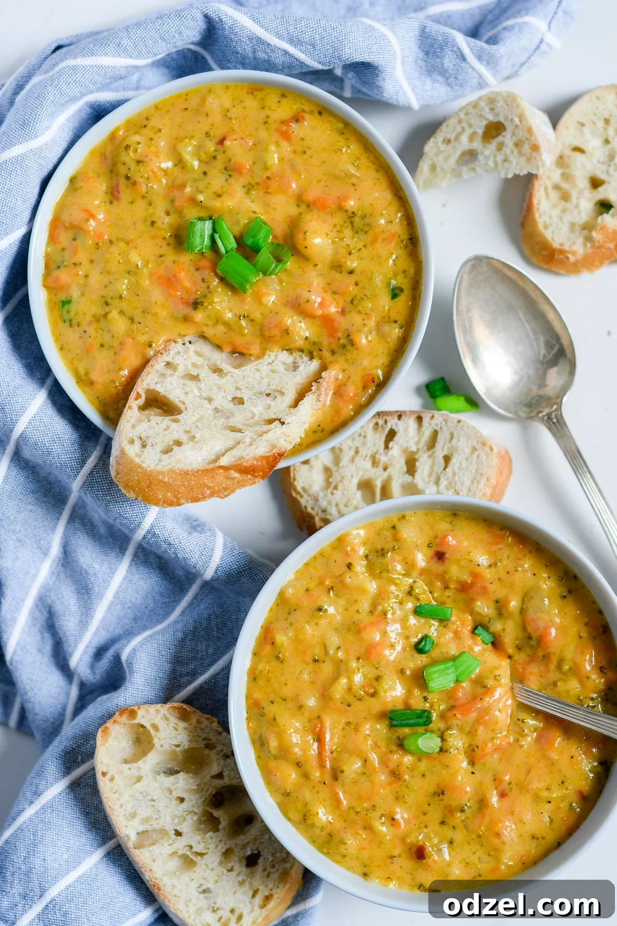 Instant Pot Creamy Broccoli Cheddar Bliss 2 Two white bowls with vibrant broccoli cheddar soup, with slices of crusty Italian bread both inside one bowl and arranged on the side. A spoon rests beside one bowl, and a blue and white striped towel adds a touch of charm to the rustic kitchen backdrop.