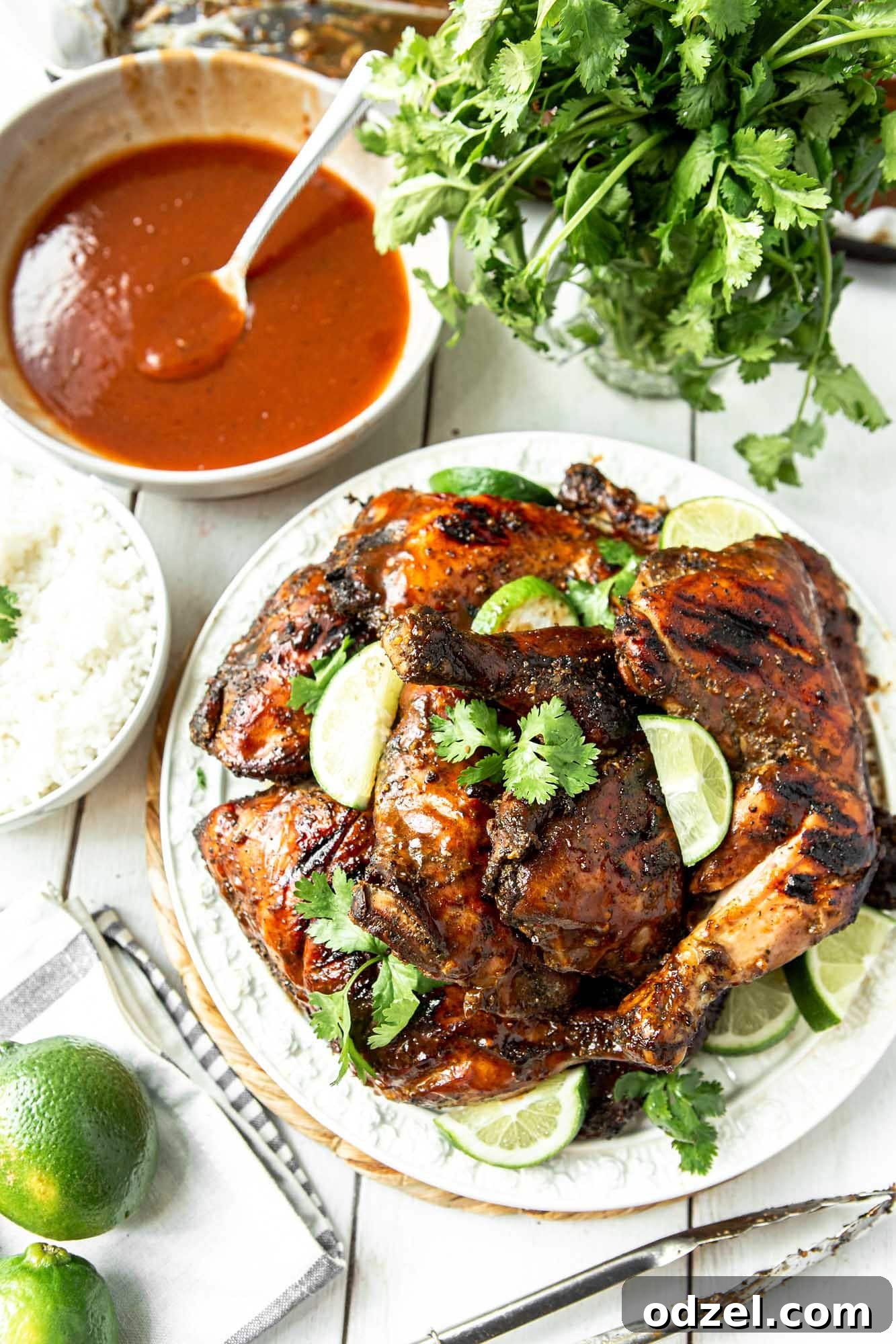 Caribbean Heat Chicken 2 Delicious Jamaican jerk chicken on a white plate with fresh cilantro and lime wedges. A side bowl of vibrant red pineapple sauce, a spoon, and more garnish are visible.