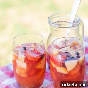 Two glasses filled with sangria and fruit on top of a red and white table cloth and a pitcher with sangria in the background.