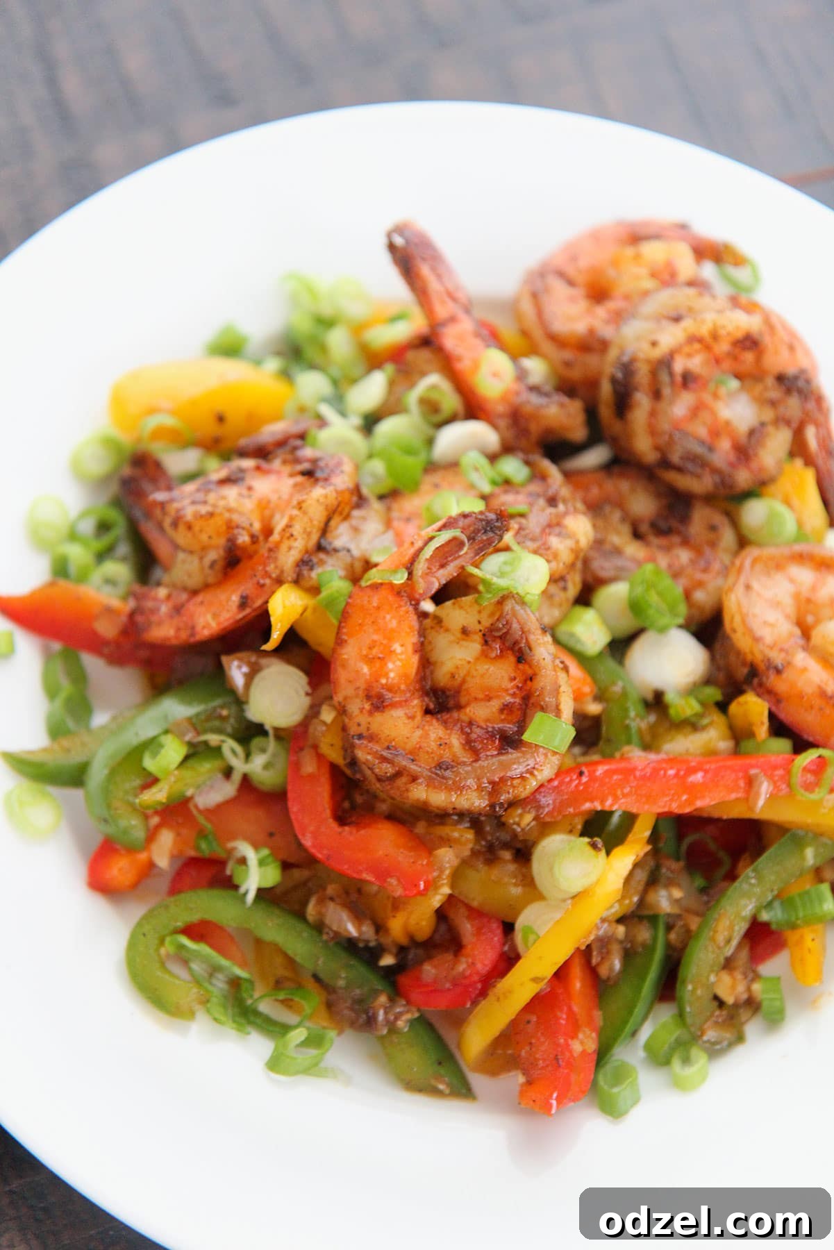 Fiery Jerk Shrimp 2 A close-up of Caribbean jerk shrimp with colorful bell peppers and onions, served on a pristine white plate.