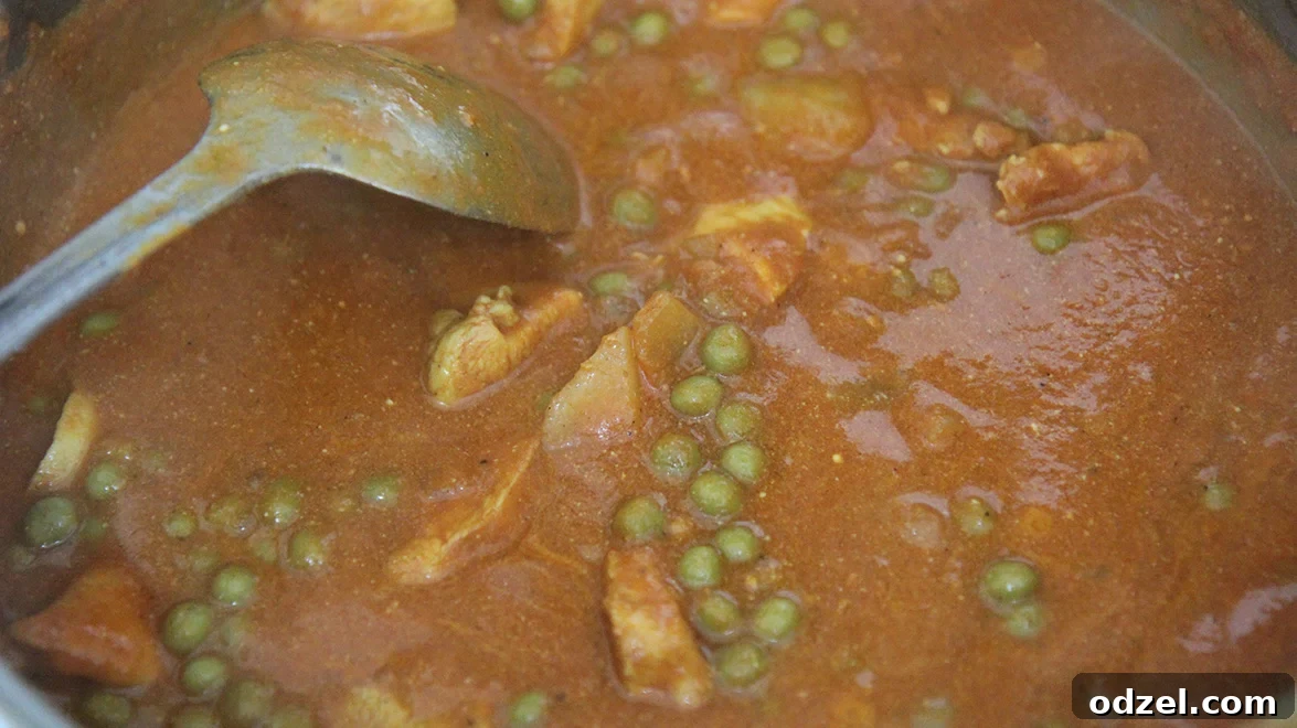 Velvet Coconut Chicken Curry 4 A vibrant coconut chicken curry simmering in a large stainless steel pot, with a spoon resting inside, showcasing its rich texture and color.