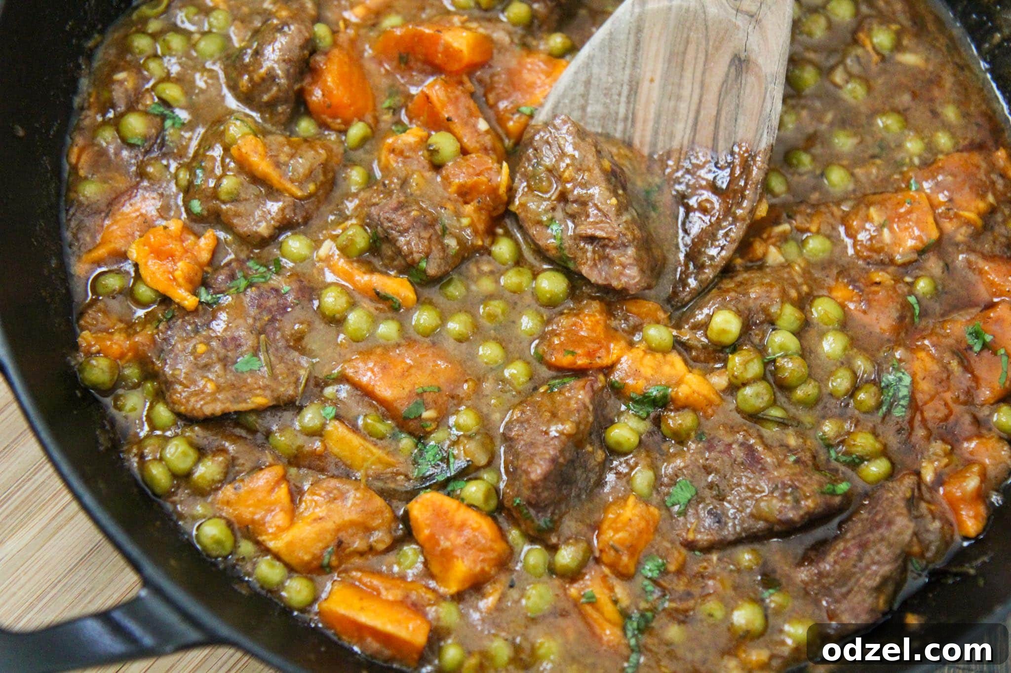 Slow-Simmered Sweet Potato Beef Delight 3 Close-up of tender beef and vibrant sweet potatoes simmering in a rich, dark sauce within a black cast iron skillet, garnished with fresh herbs.