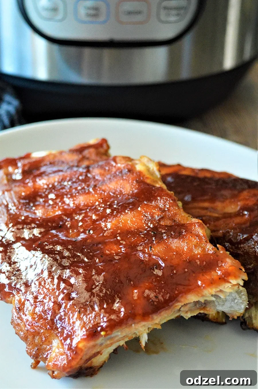 Two racks of glistening BBQ ribs on a white plate, close up, ready to be served.