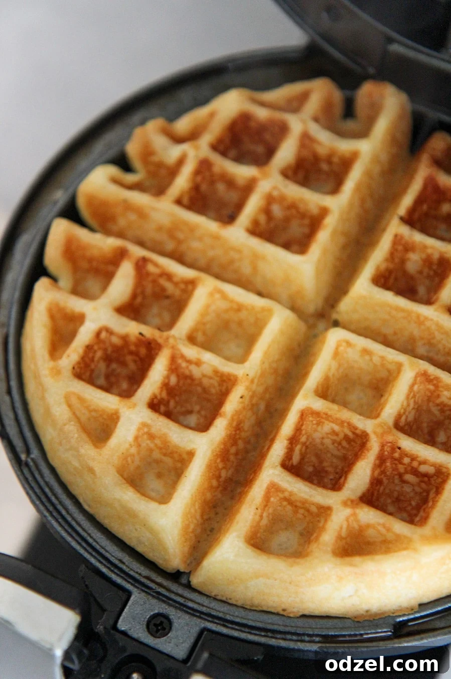 Golden Buttermilk Belgian Bliss 3 A cooked waffle resting perfectly in a waffle iron, showcasing its golden-brown texture and deep pockets.
