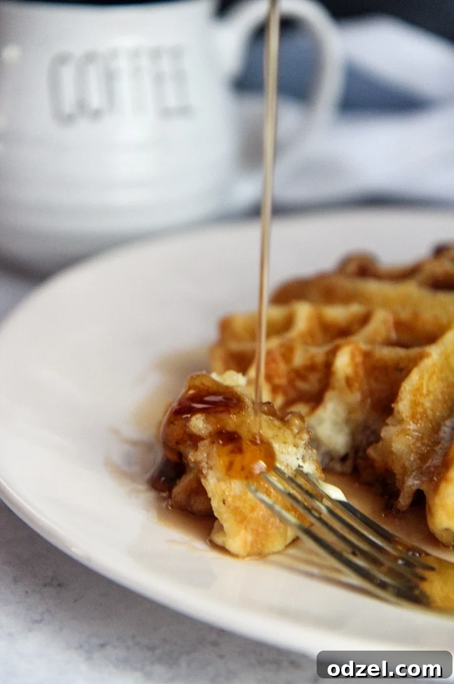 Golden Buttermilk Belgian Bliss 4 Syrup being poured generously over a piece of fluffy waffle, with a fork poised on the side, highlighting the deliciousness.