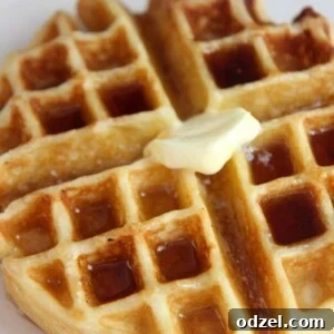 Golden Buttermilk Belgian Bliss 5 Close-up of a buttermilk waffle with syrup and butter on a white plate, highlighting its texture.