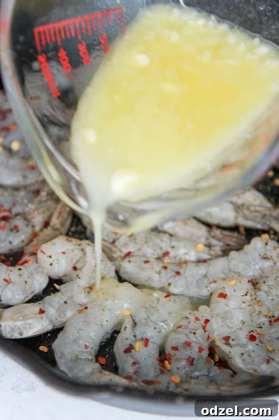 Golden Garlic Shrimp Bake 3 A measuring cup pouring melted butter over raw shrimp in a baking dish.